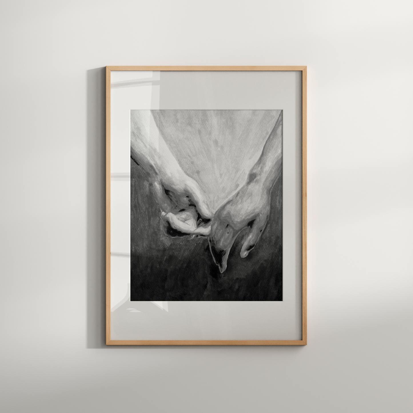 Framed black and white photograph of two hands holding each other on a light gray wall.