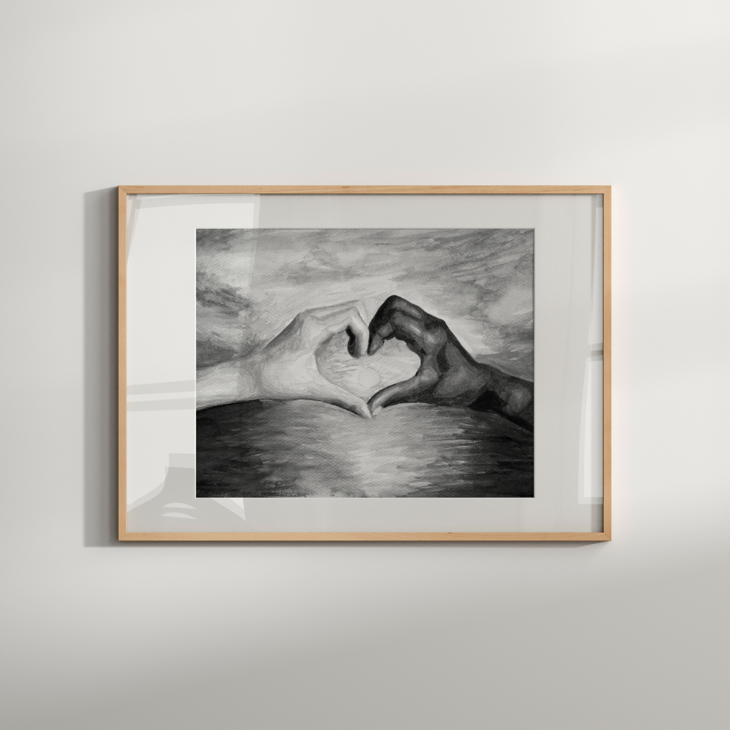 Framed black and white drawing of hands making a heart shape on a light gray wall.