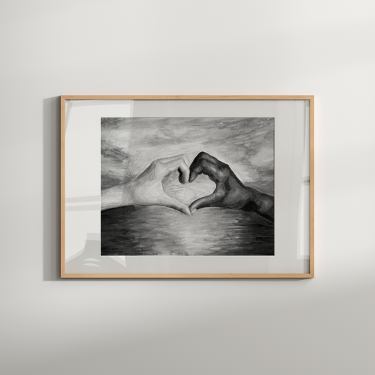 Framed black and white drawing of hands making a heart shape on a light gray wall.