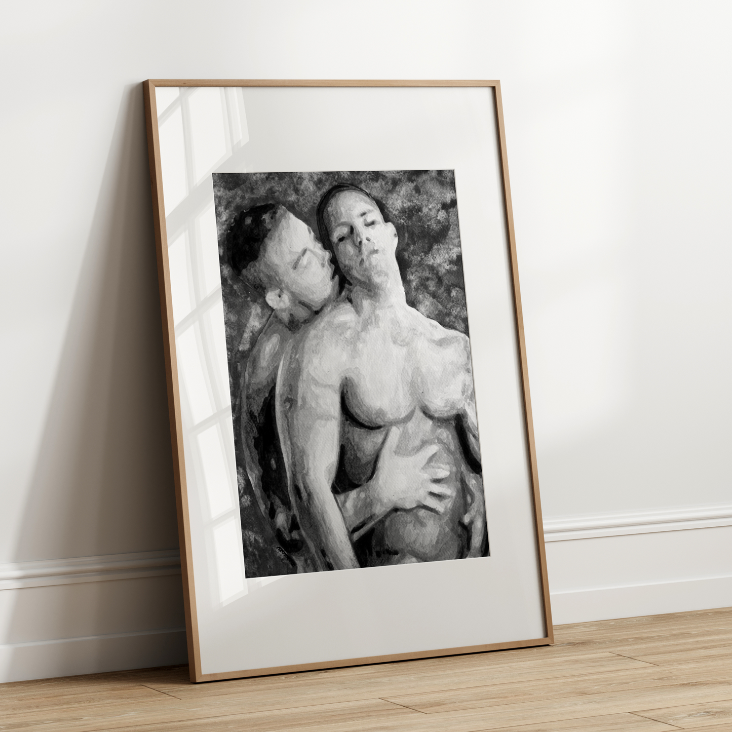 Framed black and white artwork of two people embracing on a wooden floor against a white wall.