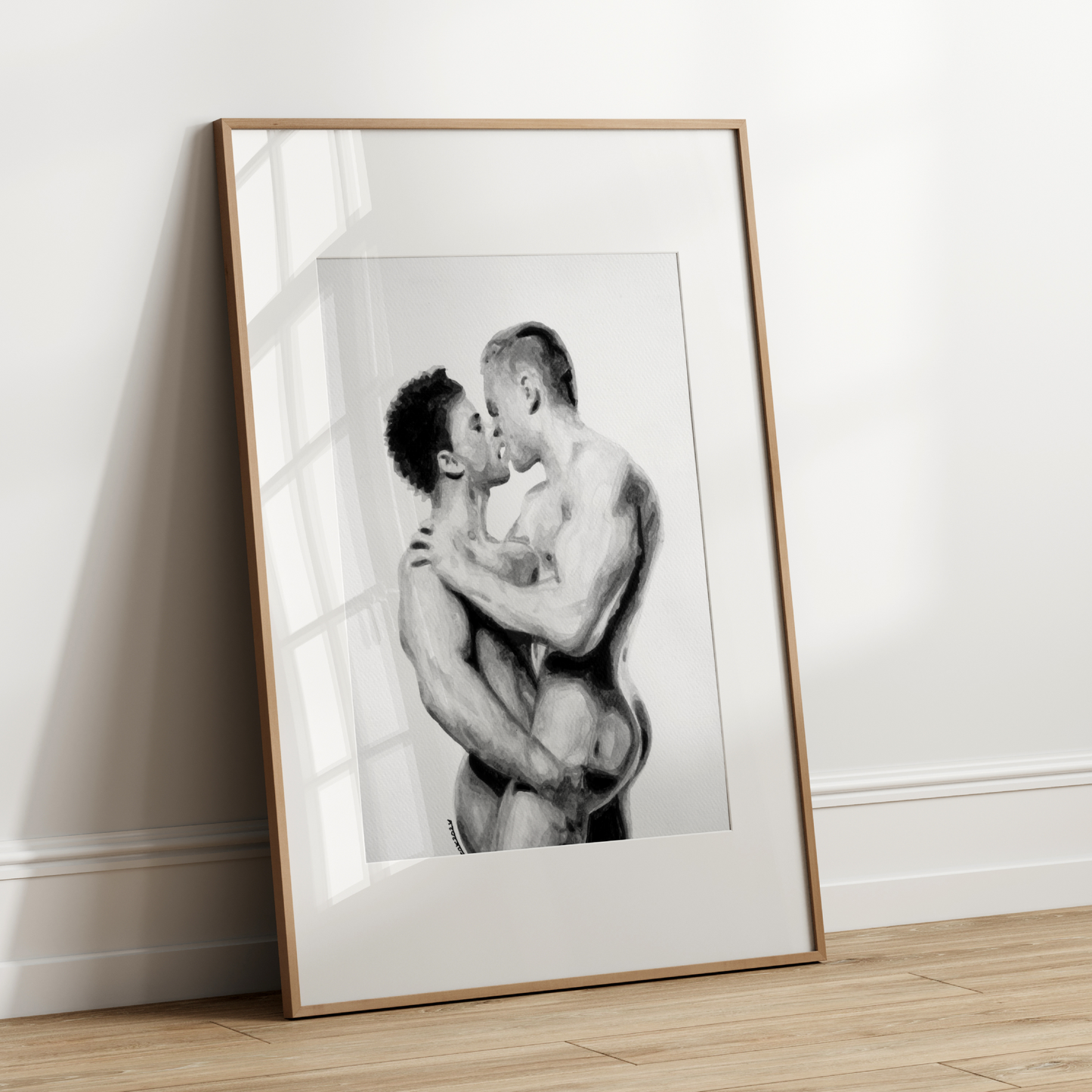 Framed black and white artwork of two people embracing on a wooden floor against a white wall.