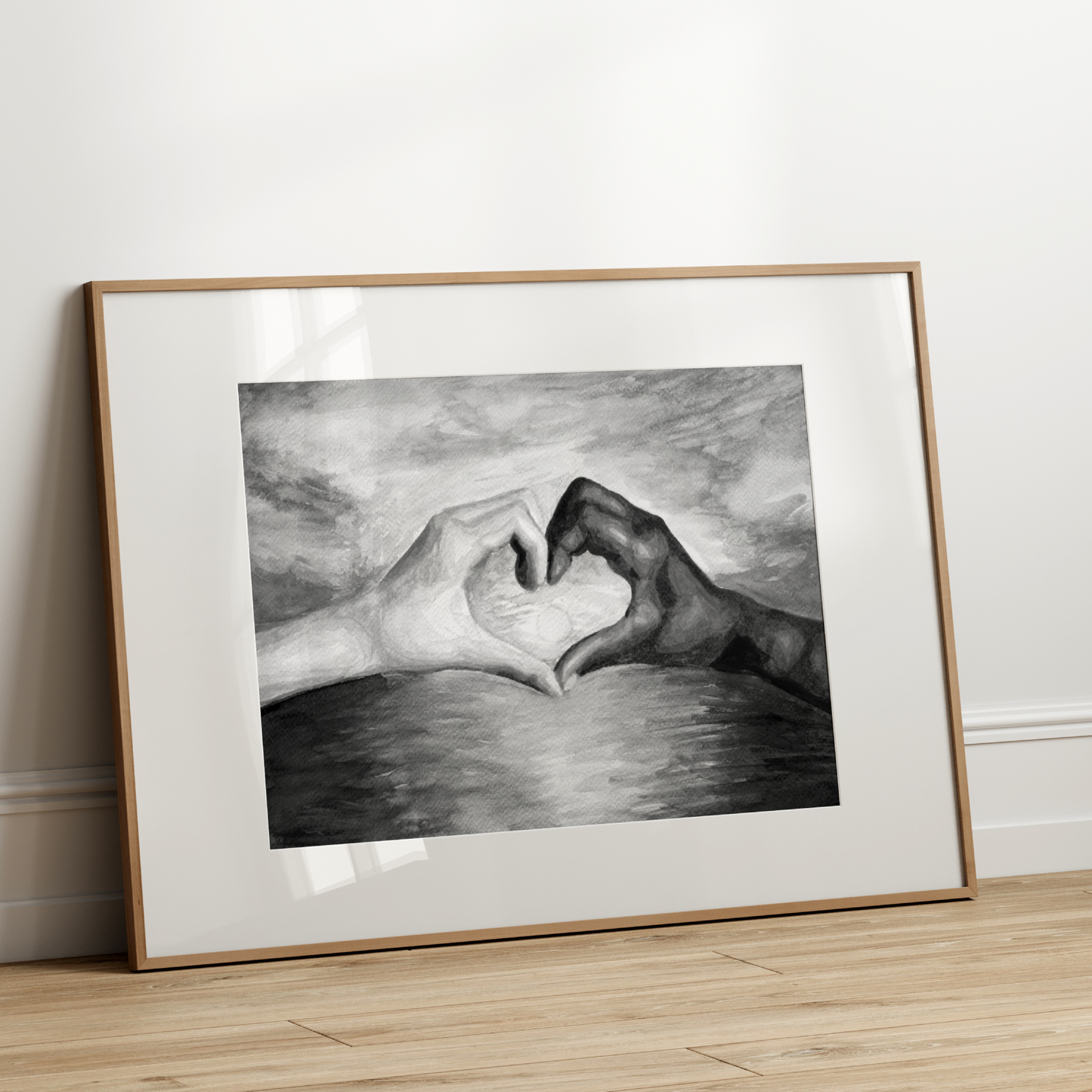 Framed artwork of two hands making a heart shape on a white wall.
