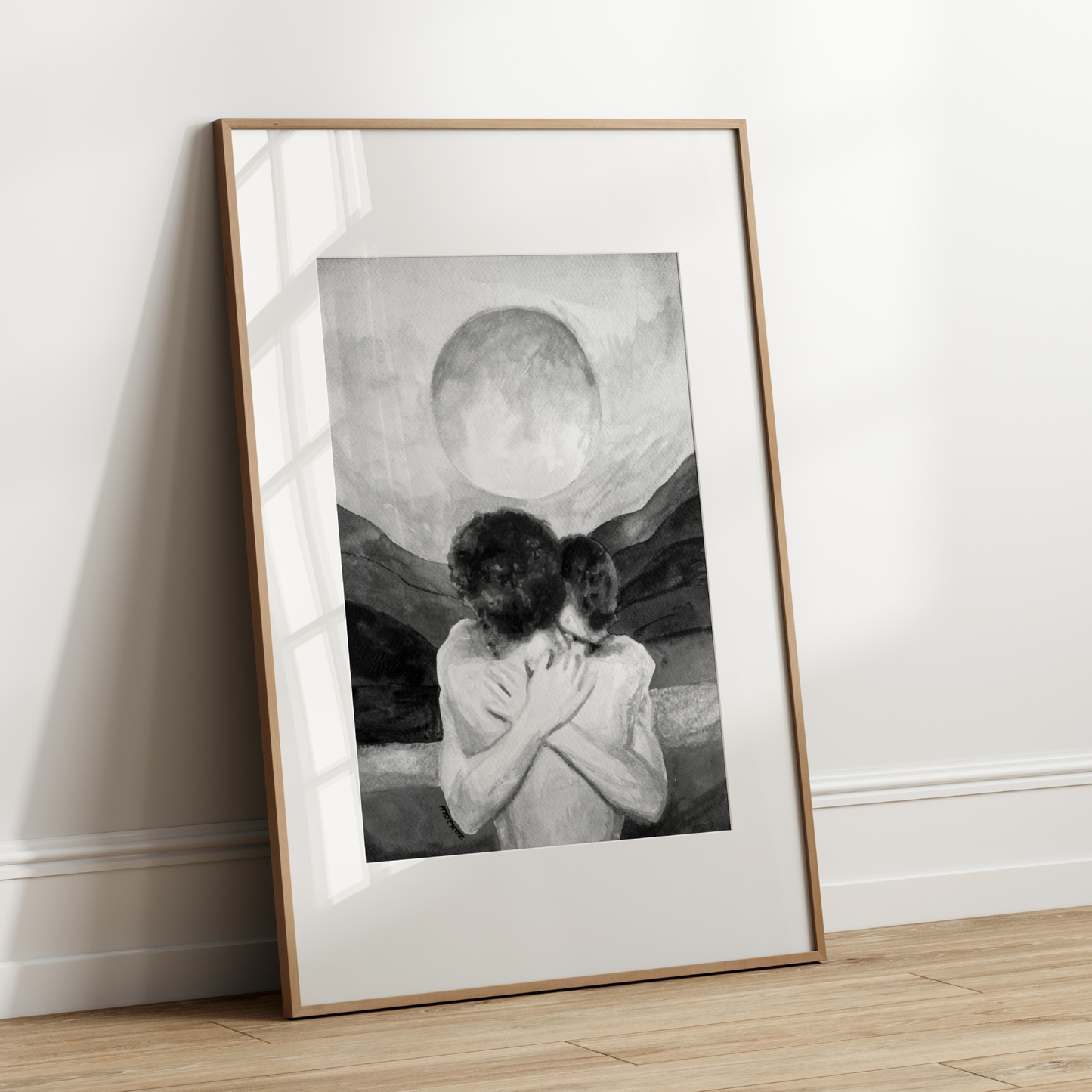 Framed black and white artwork of two people embracing against a moonlit sky on a wooden floor.