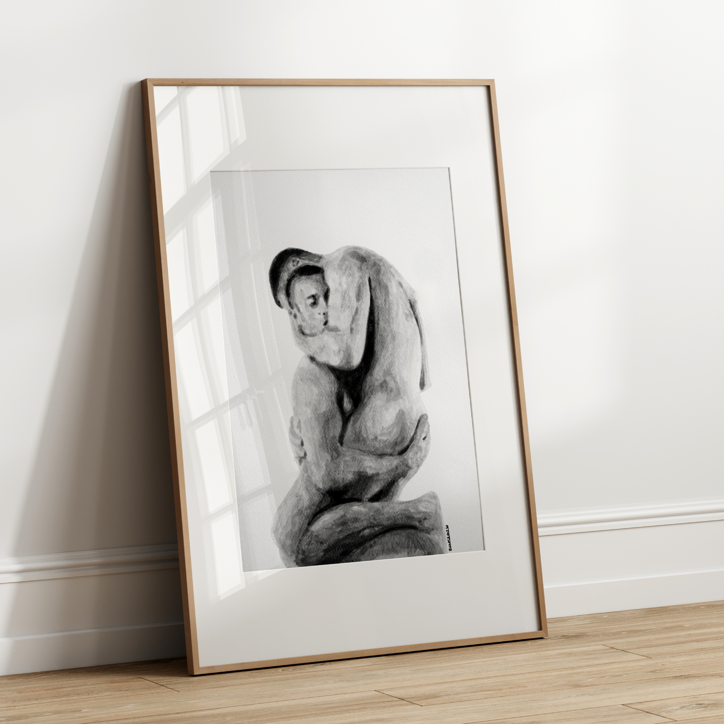 Framed black and white artwork of a seated figure leaning on a pillow against a white wall.