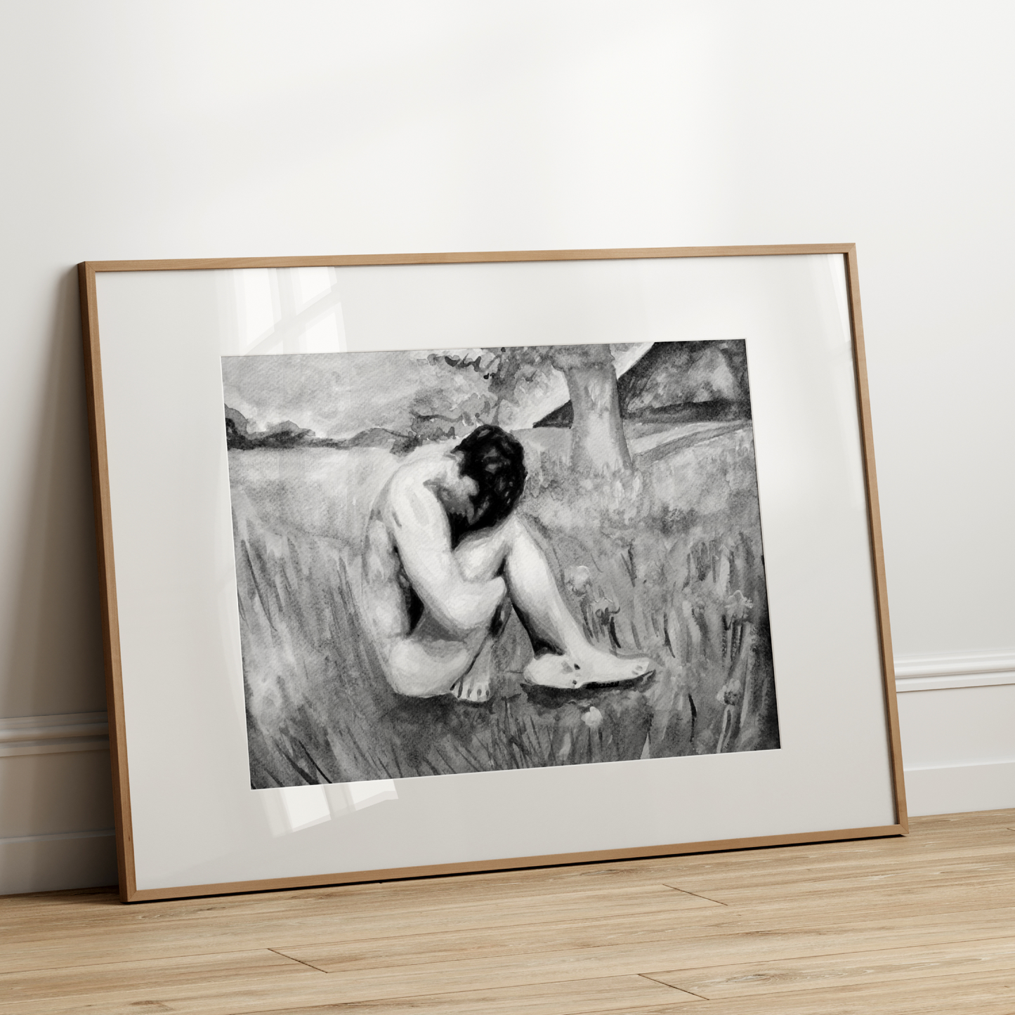 Framed black and white artwork of a nude figure sitting on a grassy bank.
