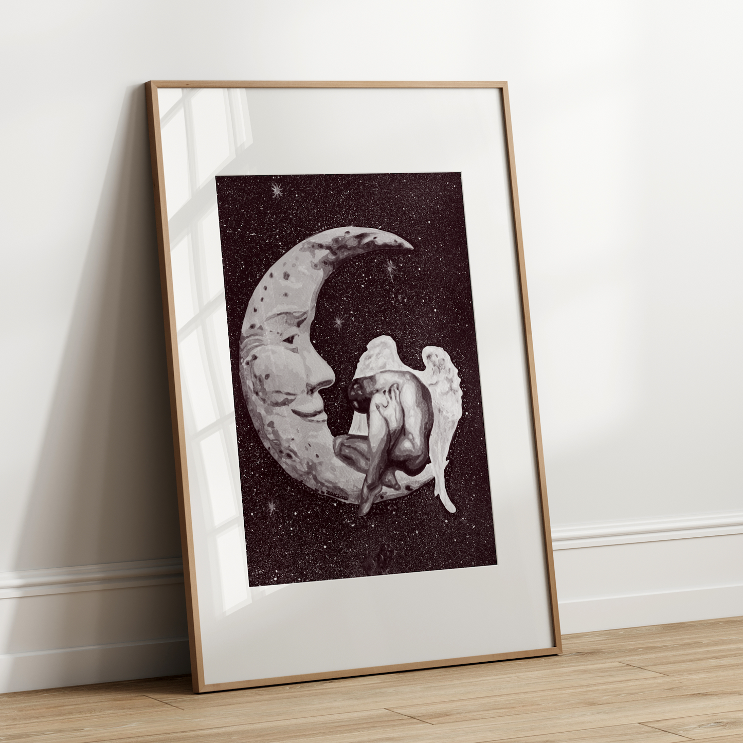 Framed artwork of a crescent moon with a person inside, leaning against a white wall.