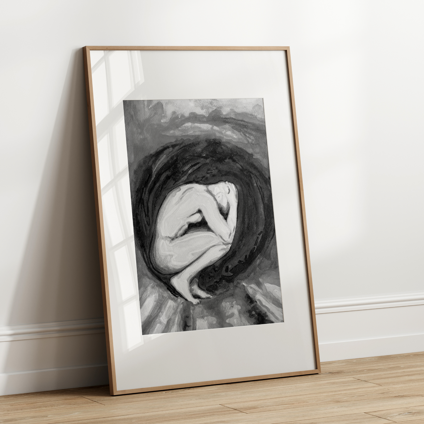 Framed black and white artwork of a woman in a womb-like shape leaning against a white wall.