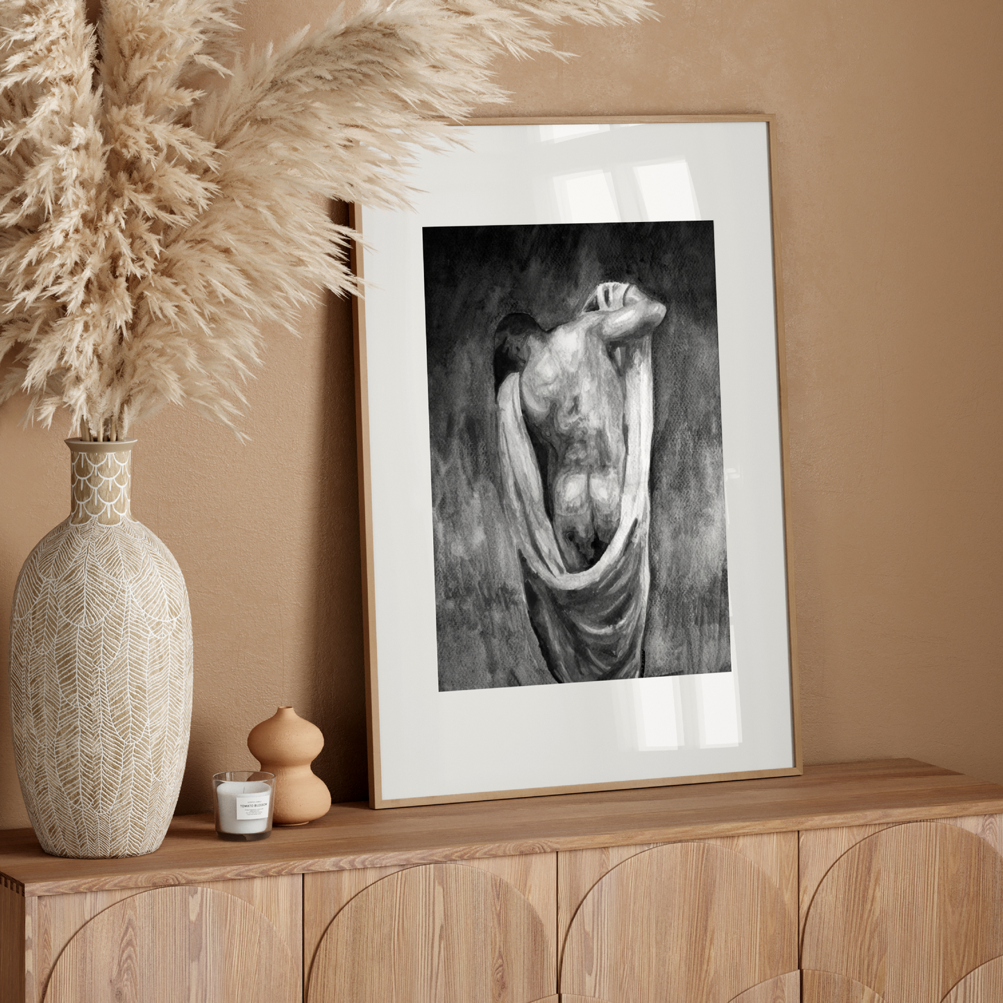Framed artwork on a wooden console table with decorative vase and pampas grass.