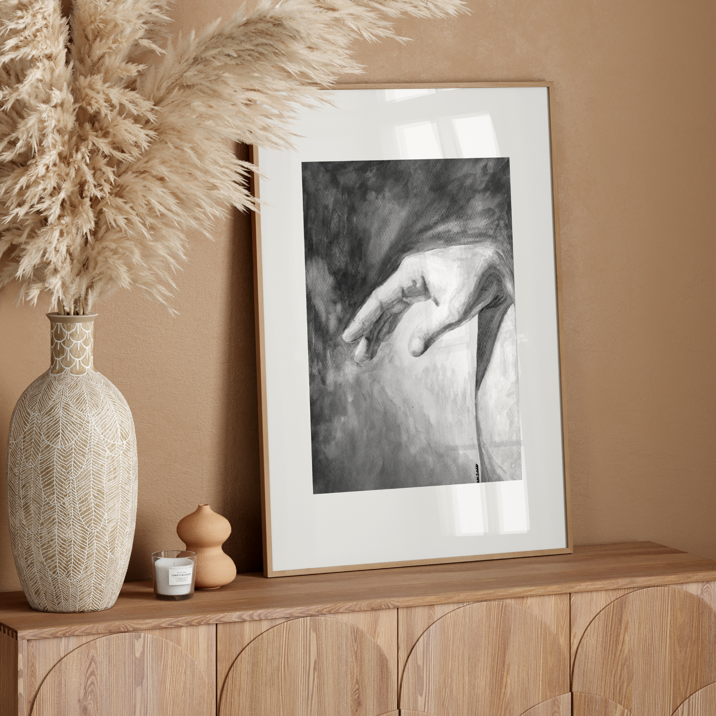 Decorative setup with a vase, candle, and framed artwork on a wooden console against a beige wall.