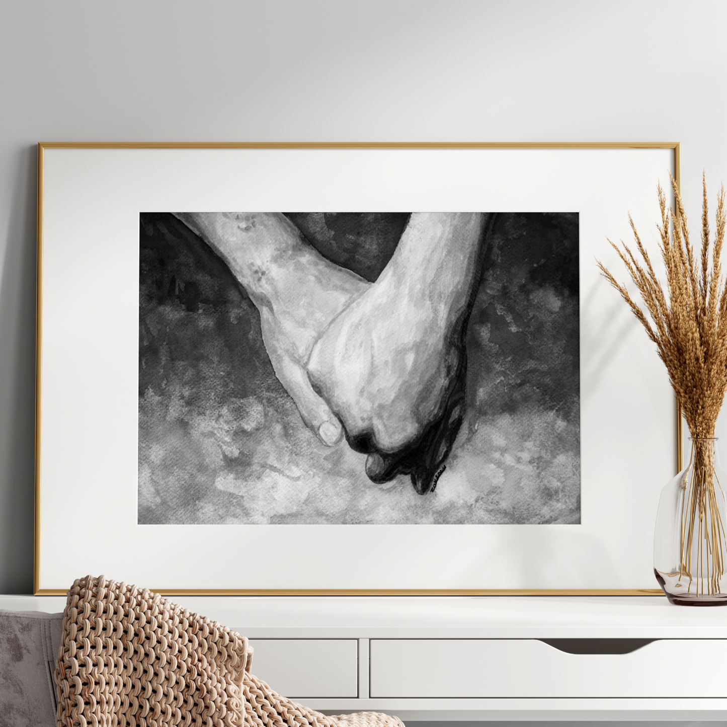 Framed black and white artwork of hands on a wall above a white console table.