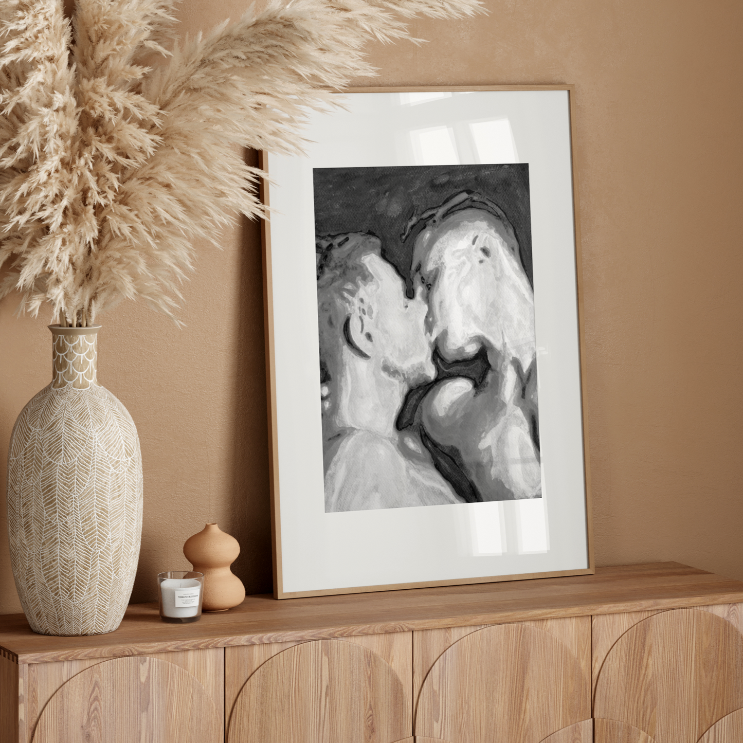 Decorative setup with a vase, candle, and framed artwork on a wooden console against a beige wall.