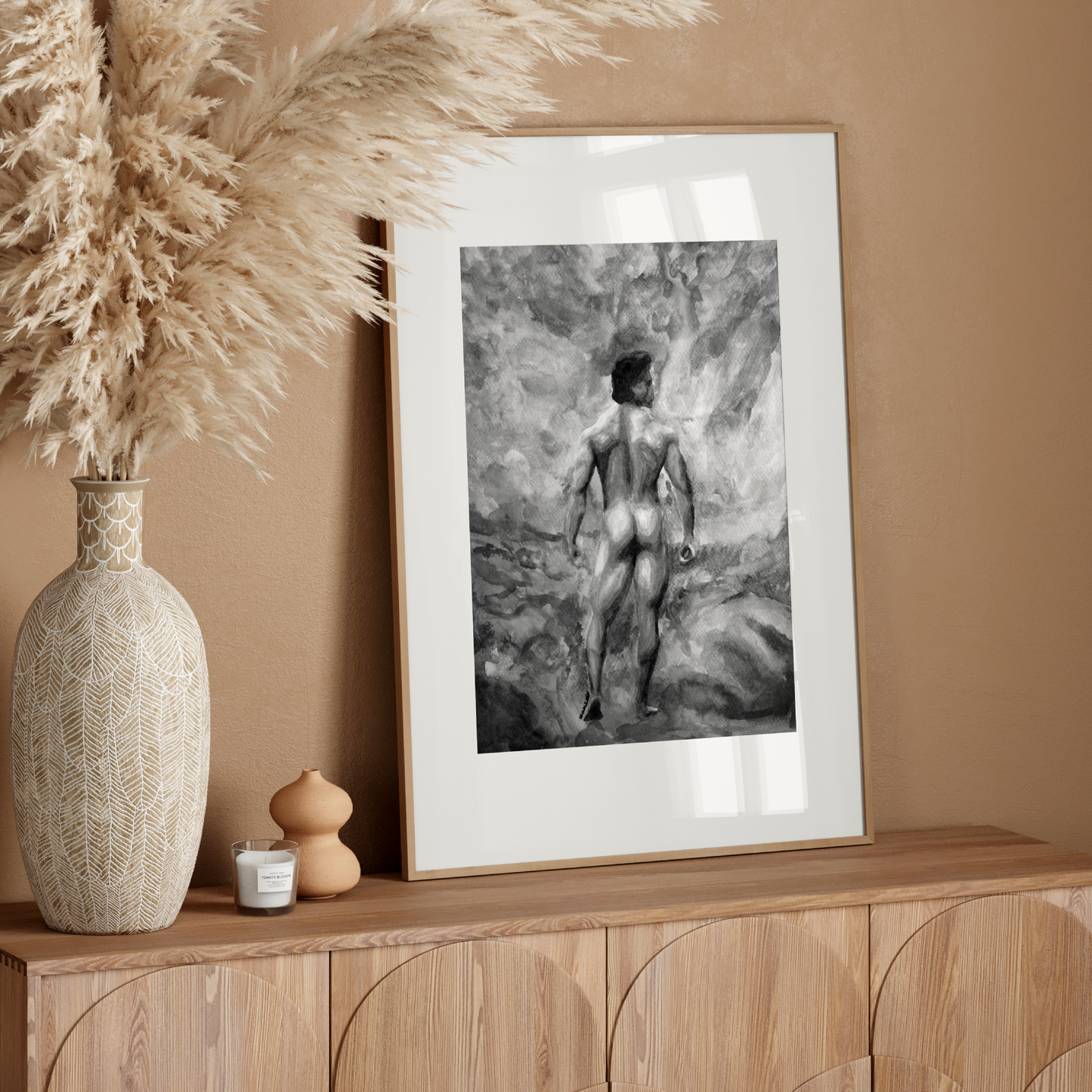 Framed artwork on a wooden console table with decorative vase and pampas grass against a beige wall.