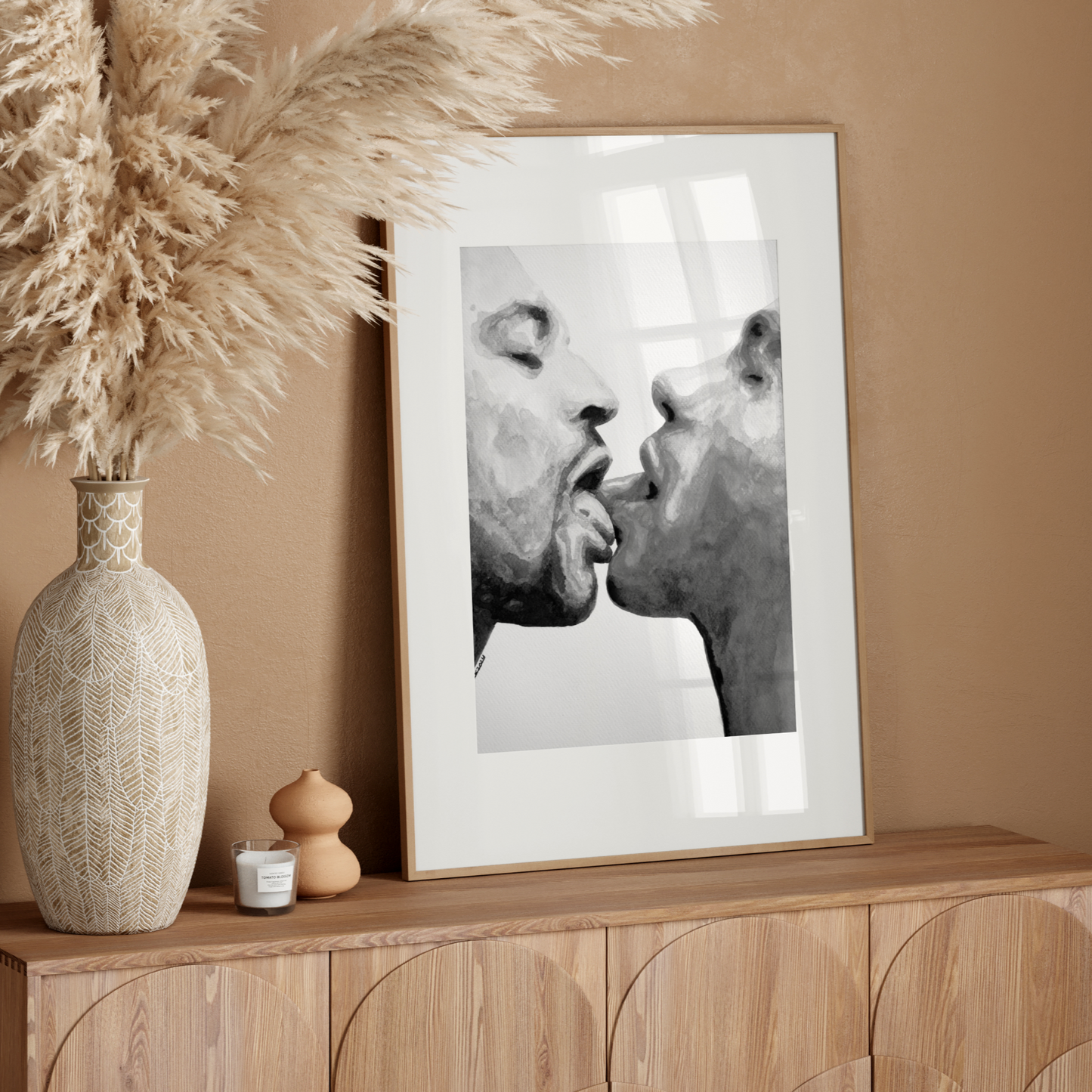 Decorative setup with a vase, candle, and framed artwork on a wooden console against a beige wall.