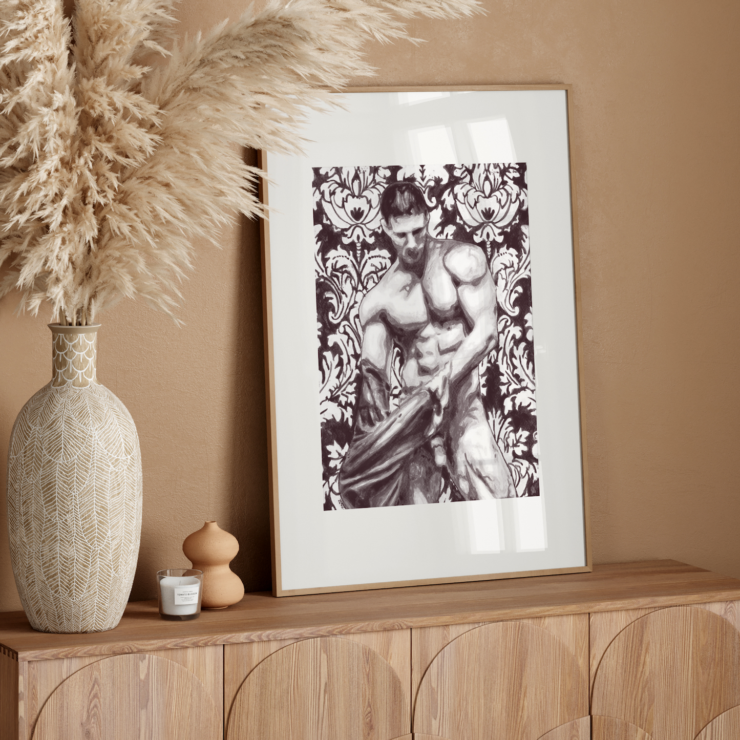 Framed artwork of a muscular figure on a wooden sideboard with decorative vase and pampas grass.
