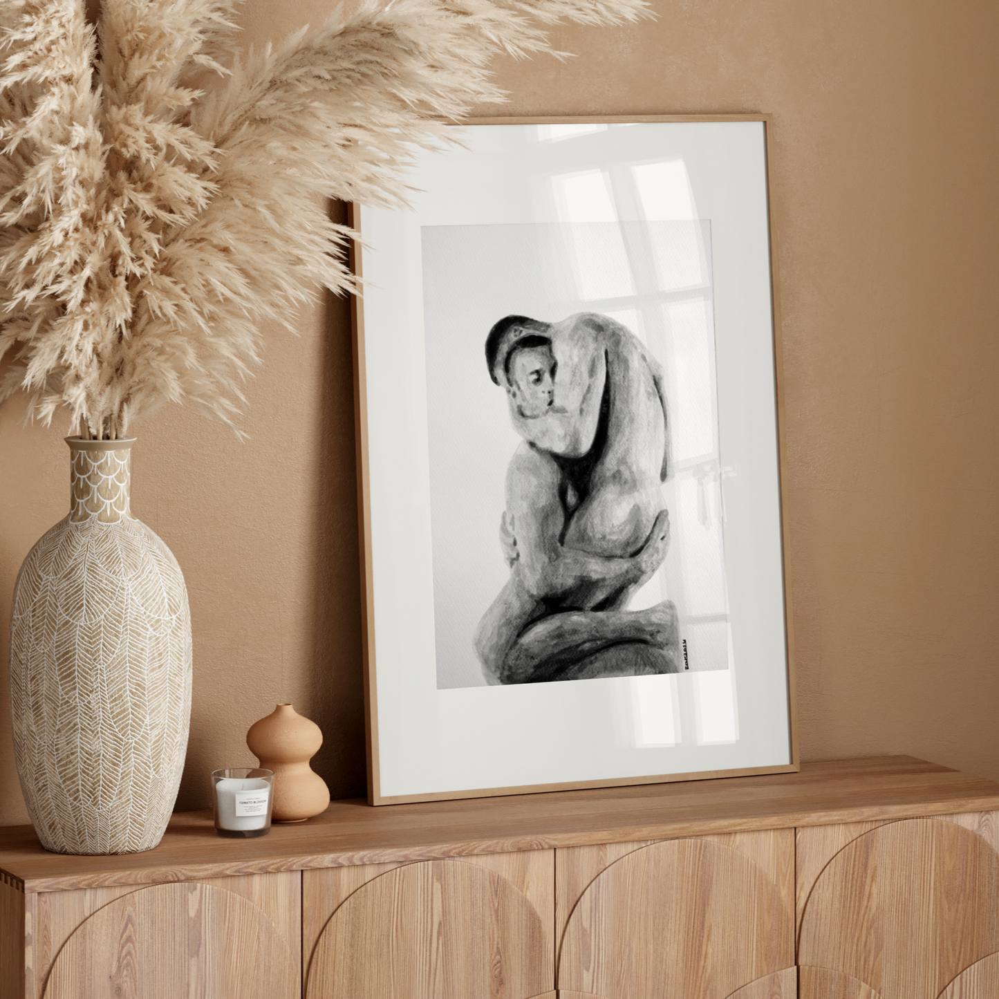 Framed black and white artwork on a wooden sideboard with decorative vase and pampas grass.