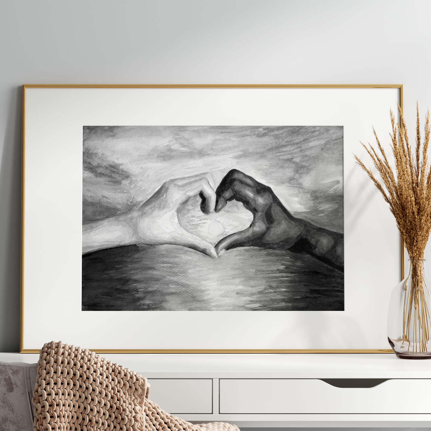 Framed black and white artwork of two hands forming a heart shape on a wall above a white console table.