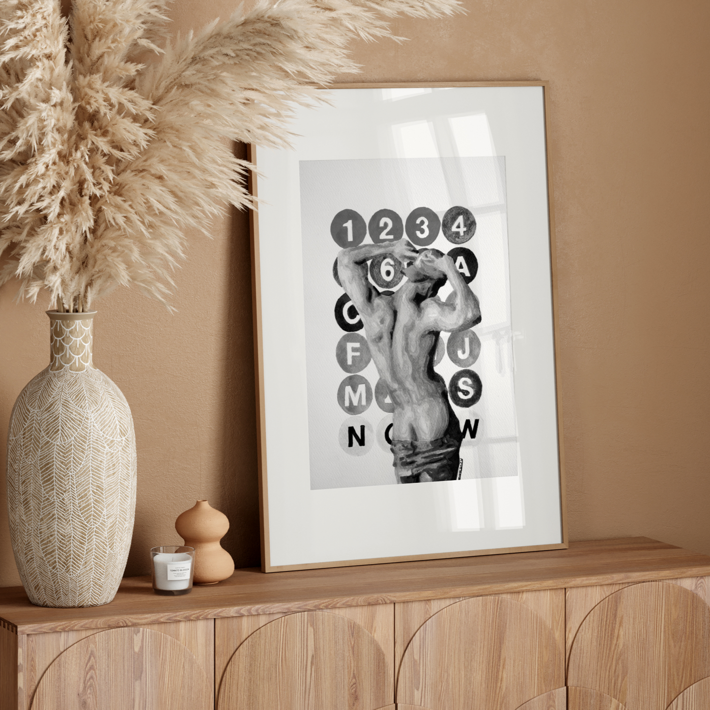 Decorative setup with a vase, candle, and framed artwork on a wooden console against a beige wall.