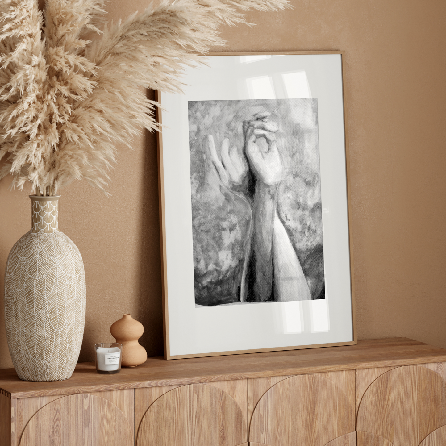 Decorative setup with a vase, dried pampas grass, and framed artwork on a wooden console against a beige wall.