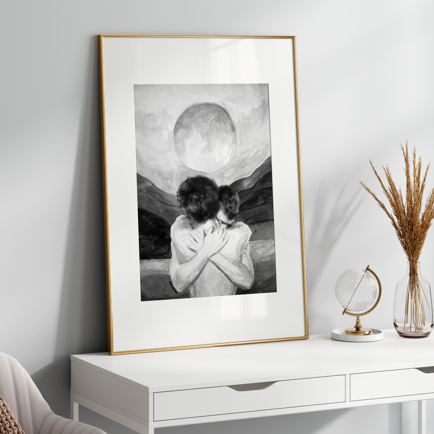 Framed artwork of two people embracing with a moon in the background on a white wall.