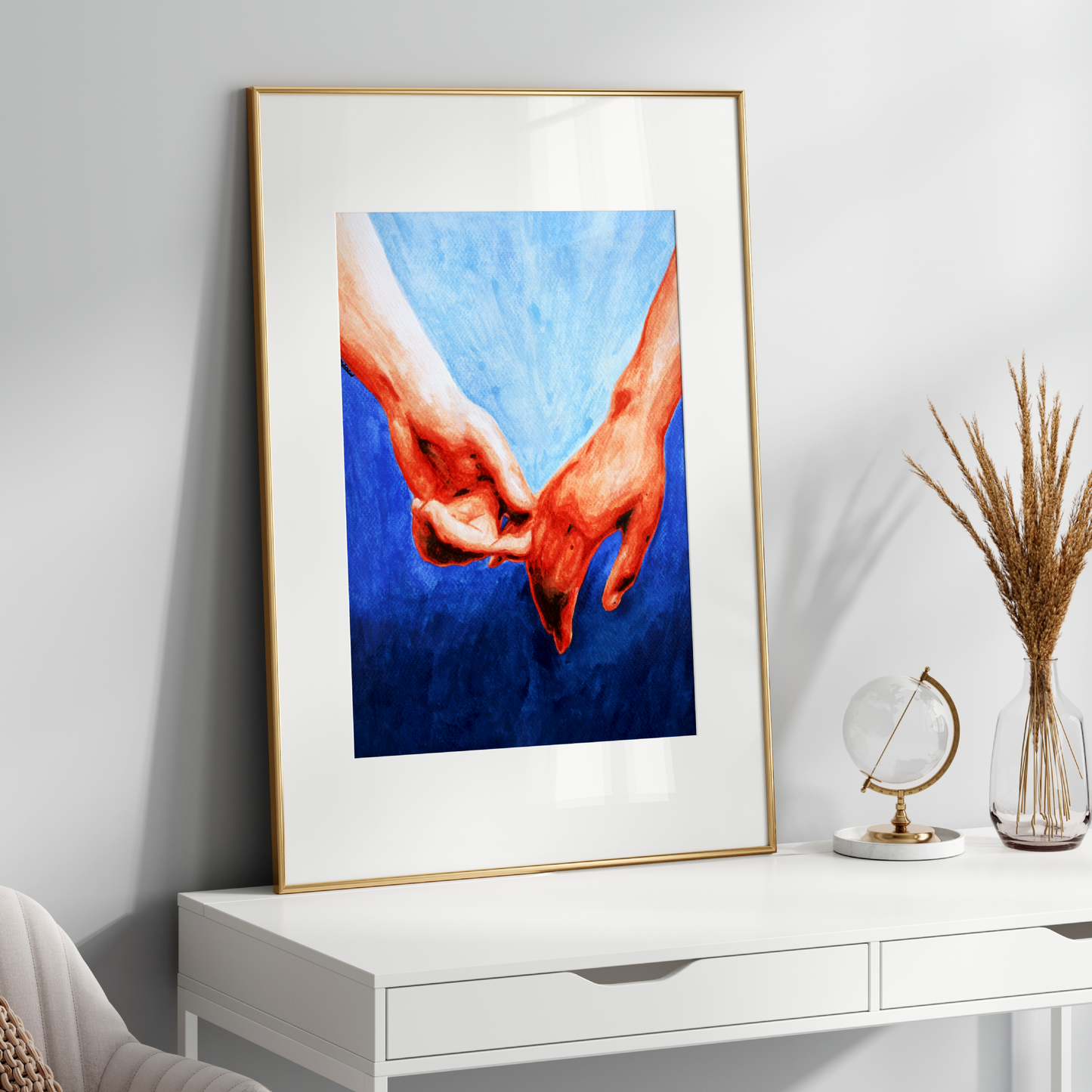 Framed artwork of hands holding a heart on a white wall above a white console table.