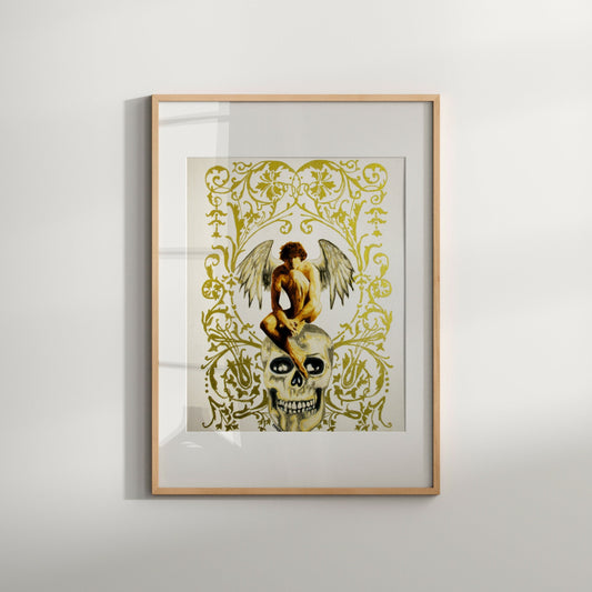 A framed art print featuring an illustration of an angel sitting on a skull, with a gold and dark color scheme and decorative elements.