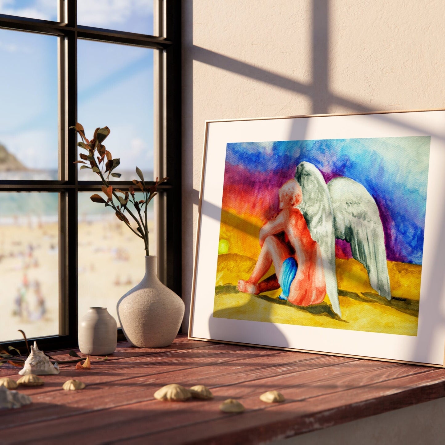 A watercolor painting of an angel sitting next to a sunset, framed in a light wood frame.