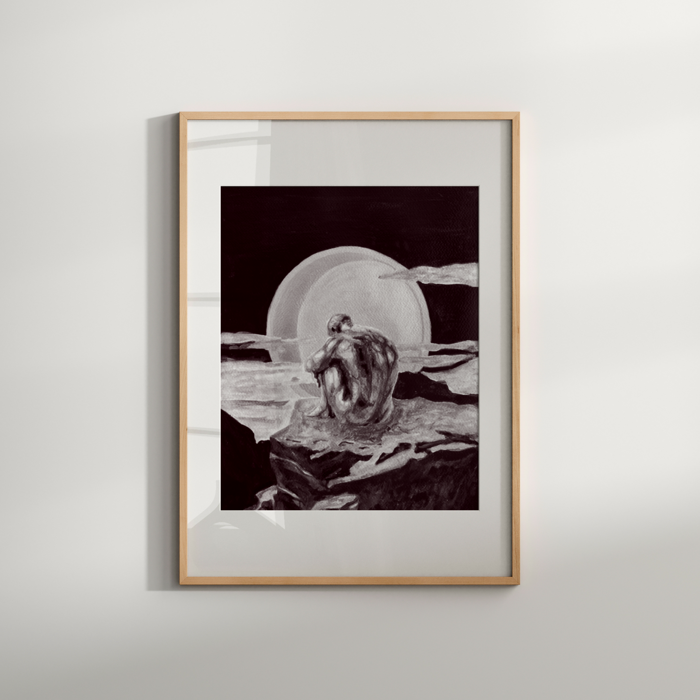 Framed black and white artwork of a person sitting on a rock with a bowl, on a light gray wall.