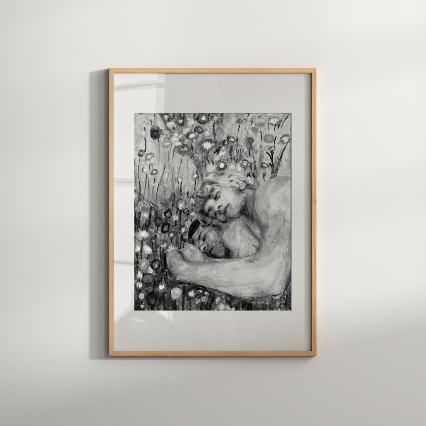 Framed black and white artwork of a woman embracing a child against a floral background on a light gray wall.