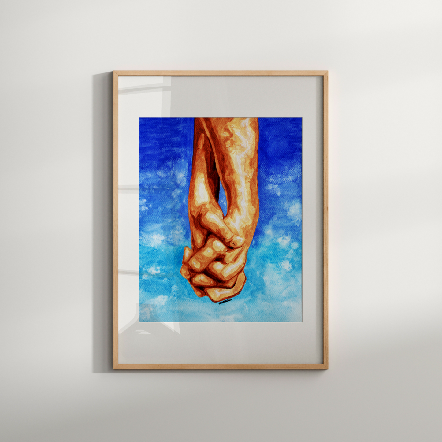 Framed artwork of clasped hands against a blue sky background on a white wall.