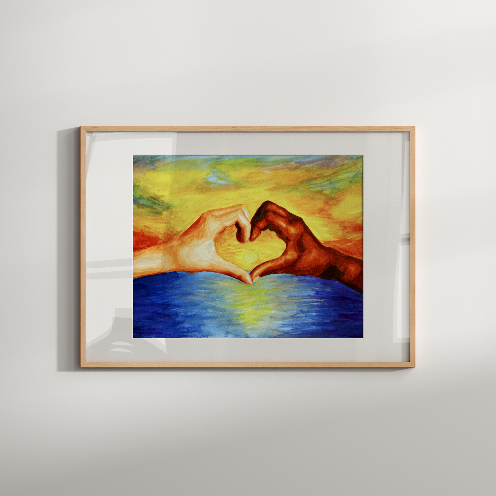 Framed artwork of two hands forming a heart shape over water on a light gray wall.
