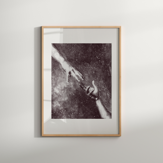 Framed artwork of two hands reaching towards each other against a starry background on a white wall.