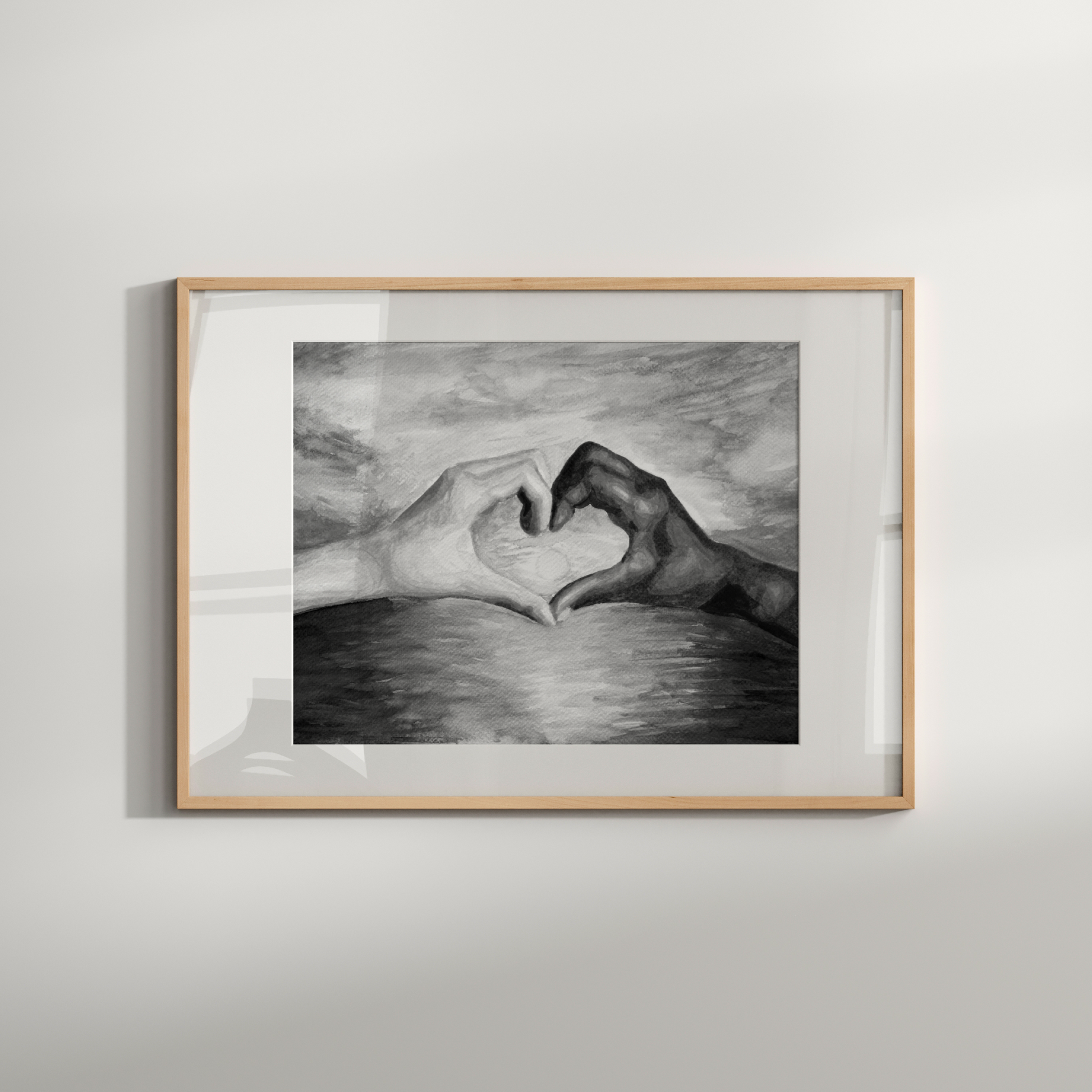 Framed black and white drawing of hands making a heart shape on a light gray wall.