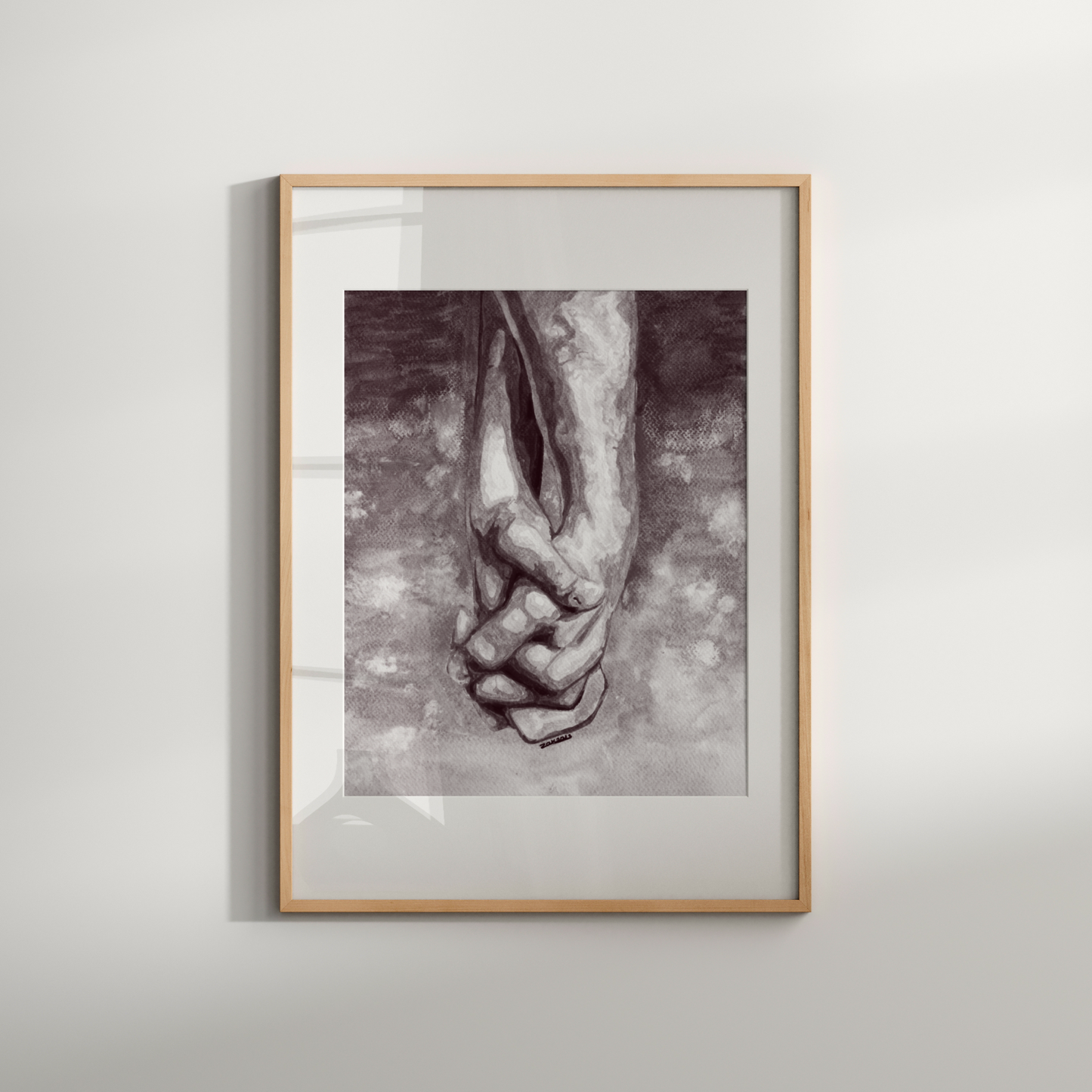 Framed artwork of two hands holding each other on a light gray wall.
