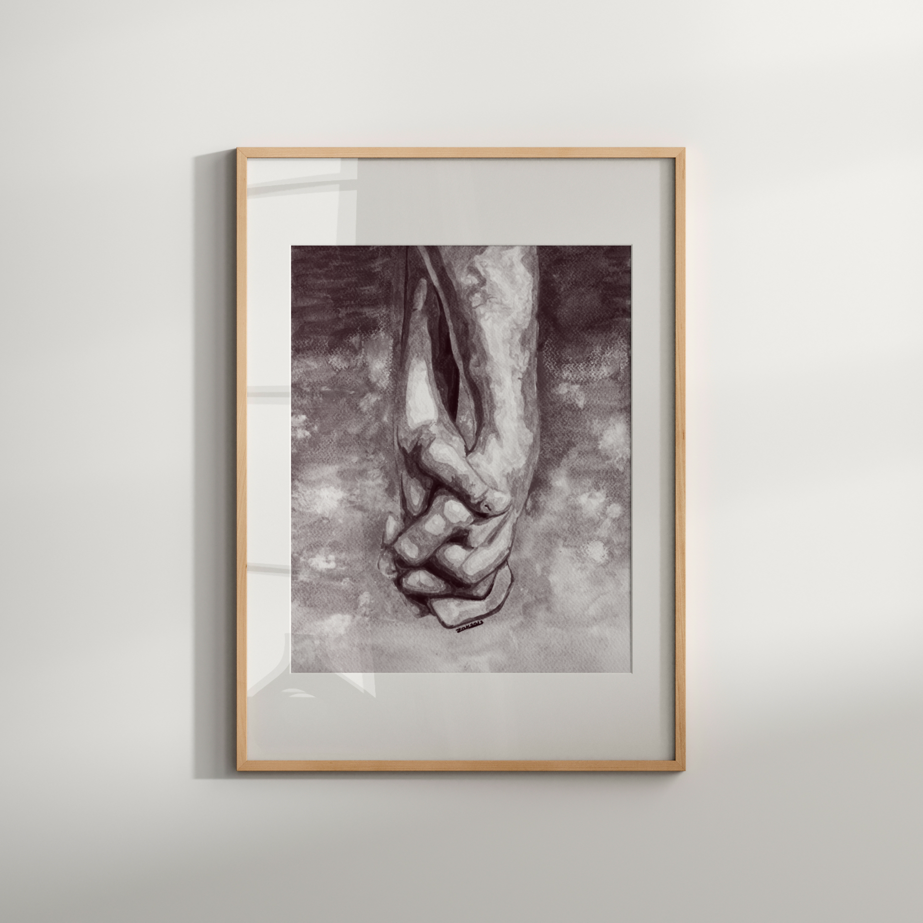 Framed artwork of two hands holding each other on a light gray wall.