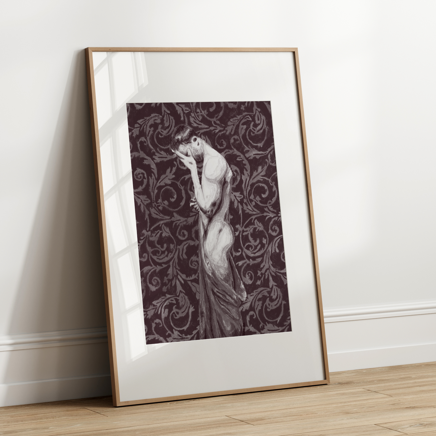 Framed artwork of a woman in a flowing dress against a decorative patterned background, leaning against a white wall.