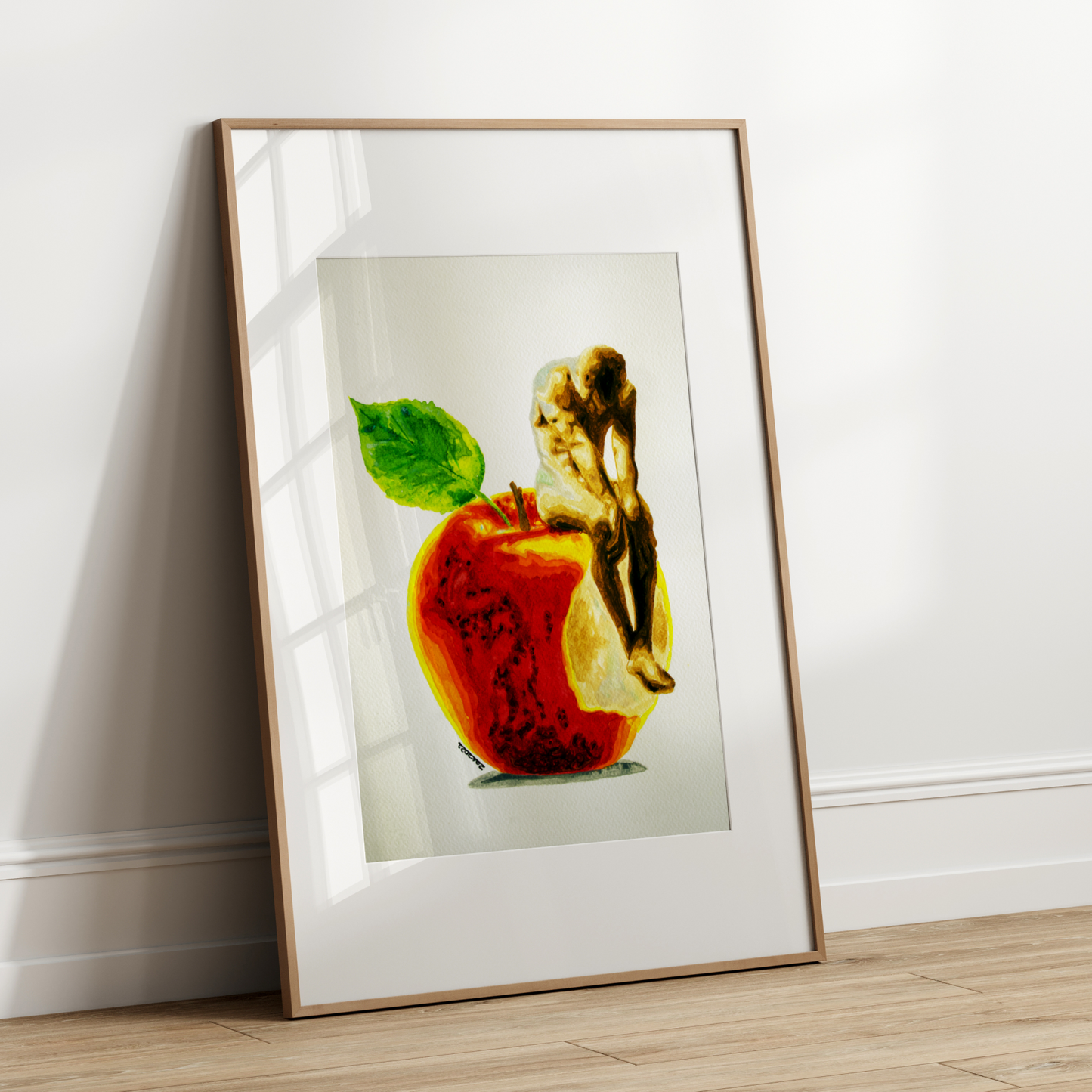 Framed artwork of a red apple with a green leaf and a gold figurine on a white wall.