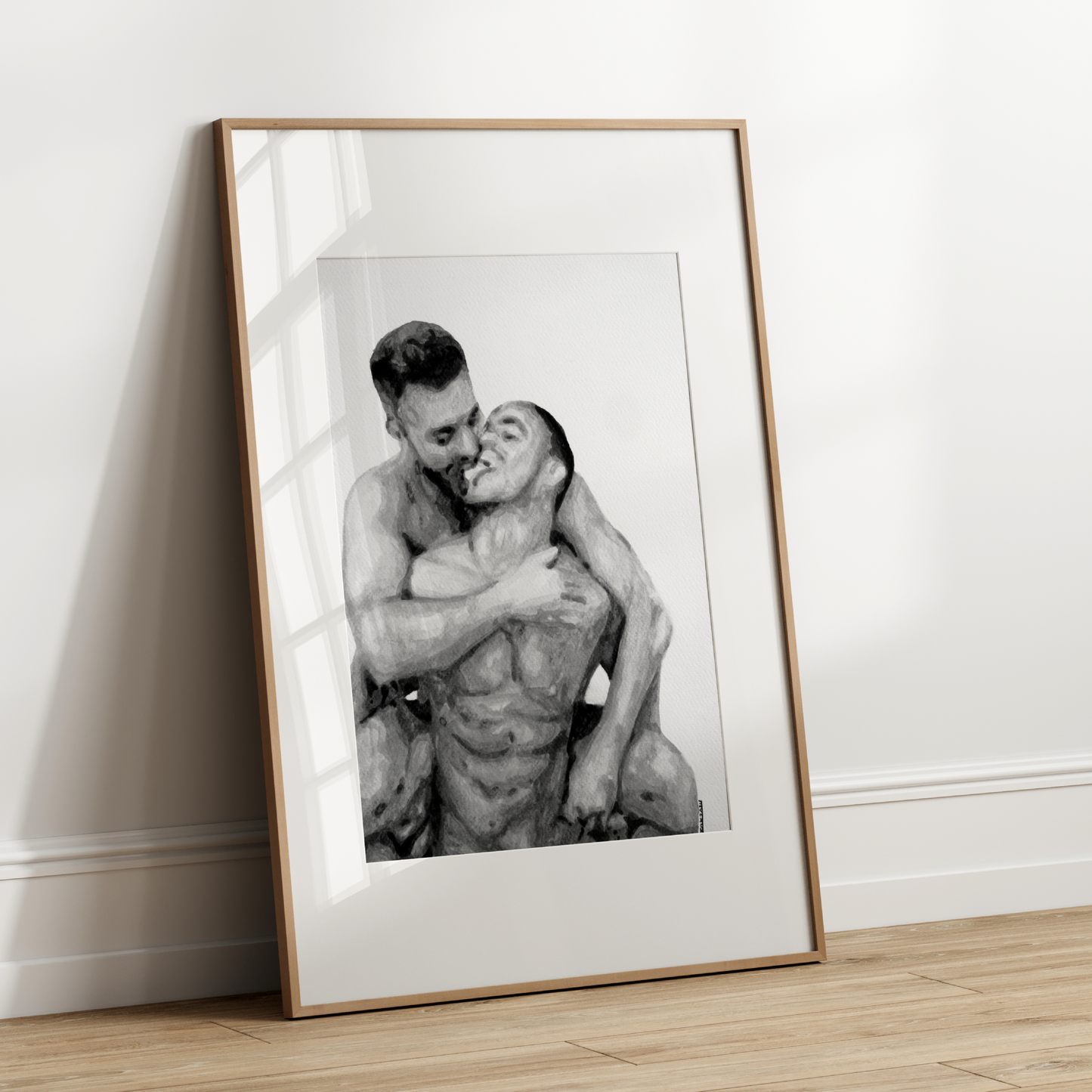 Framed black and white photograph of two people embracing on a wooden floor against a white wall.