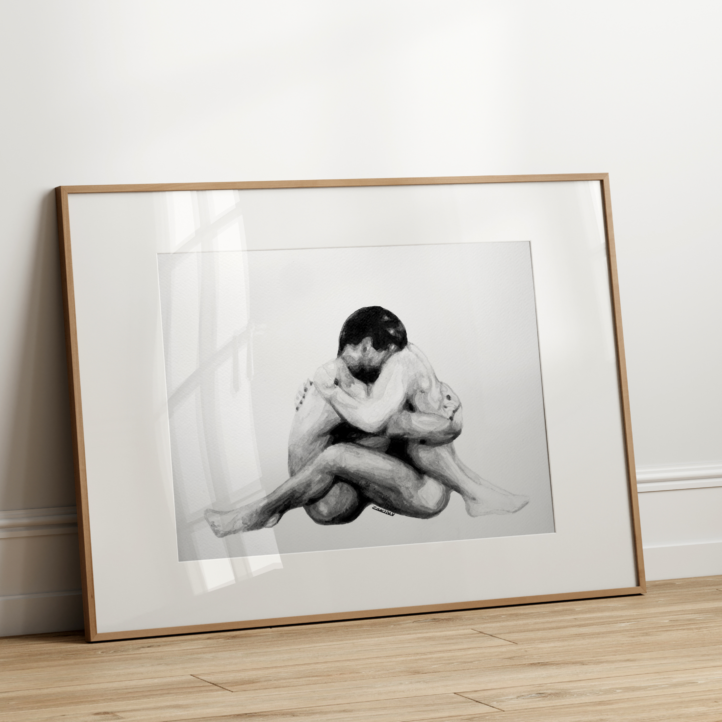 Framed black and white photograph of two people embracing on a wooden floor against a white wall.