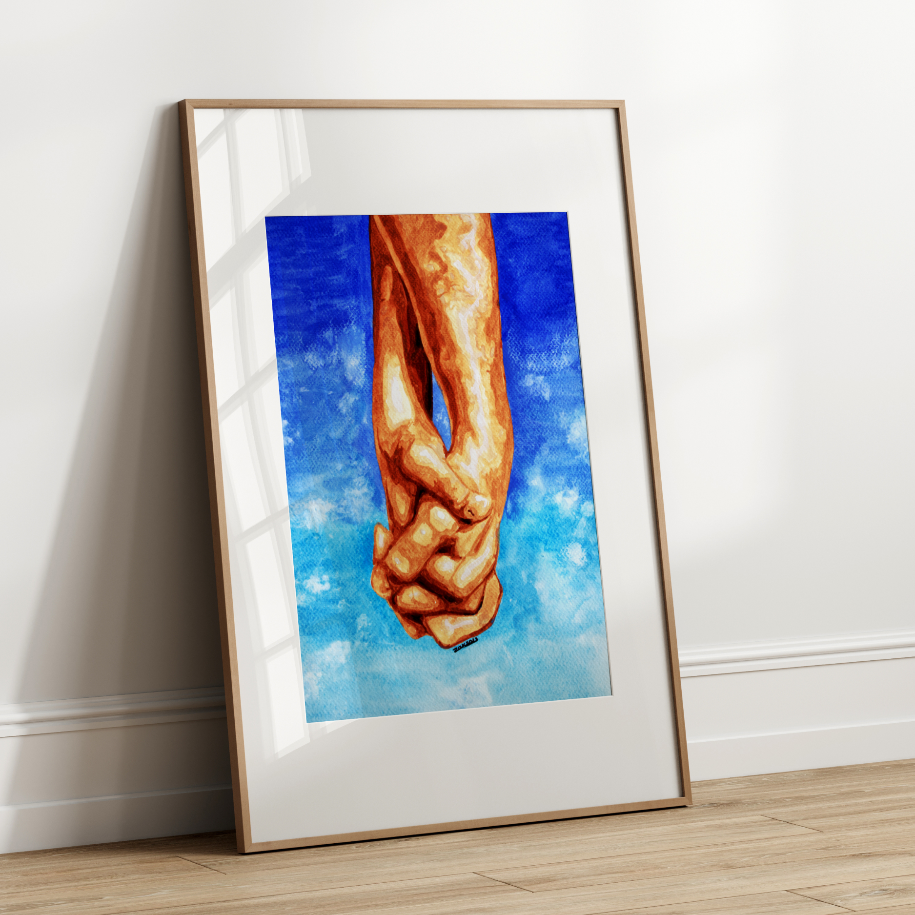 Framed artwork of two hands holding each other against a blue sky on a white wall.