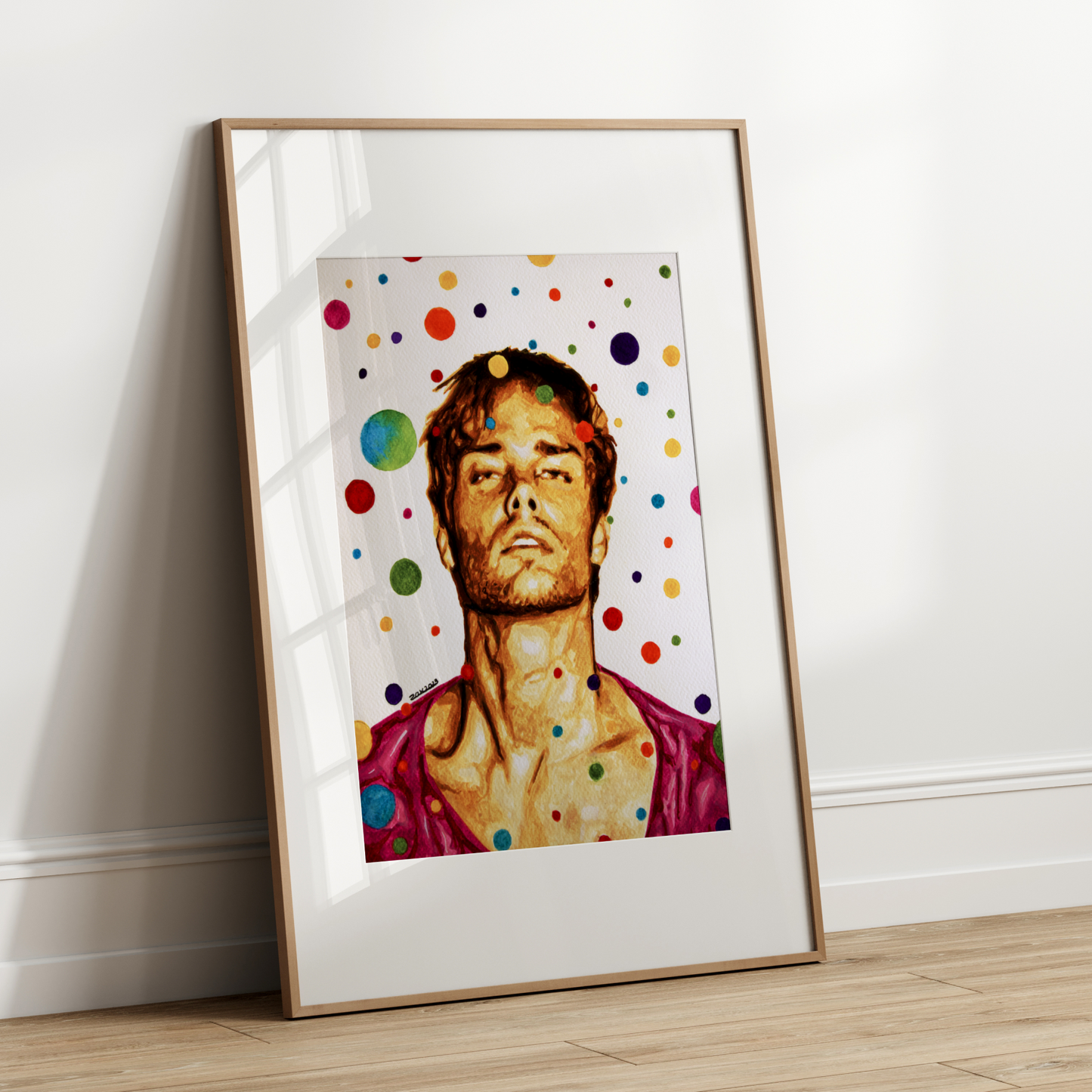 Framed artwork with a portrait of a person against a polka dot background on a white wall.