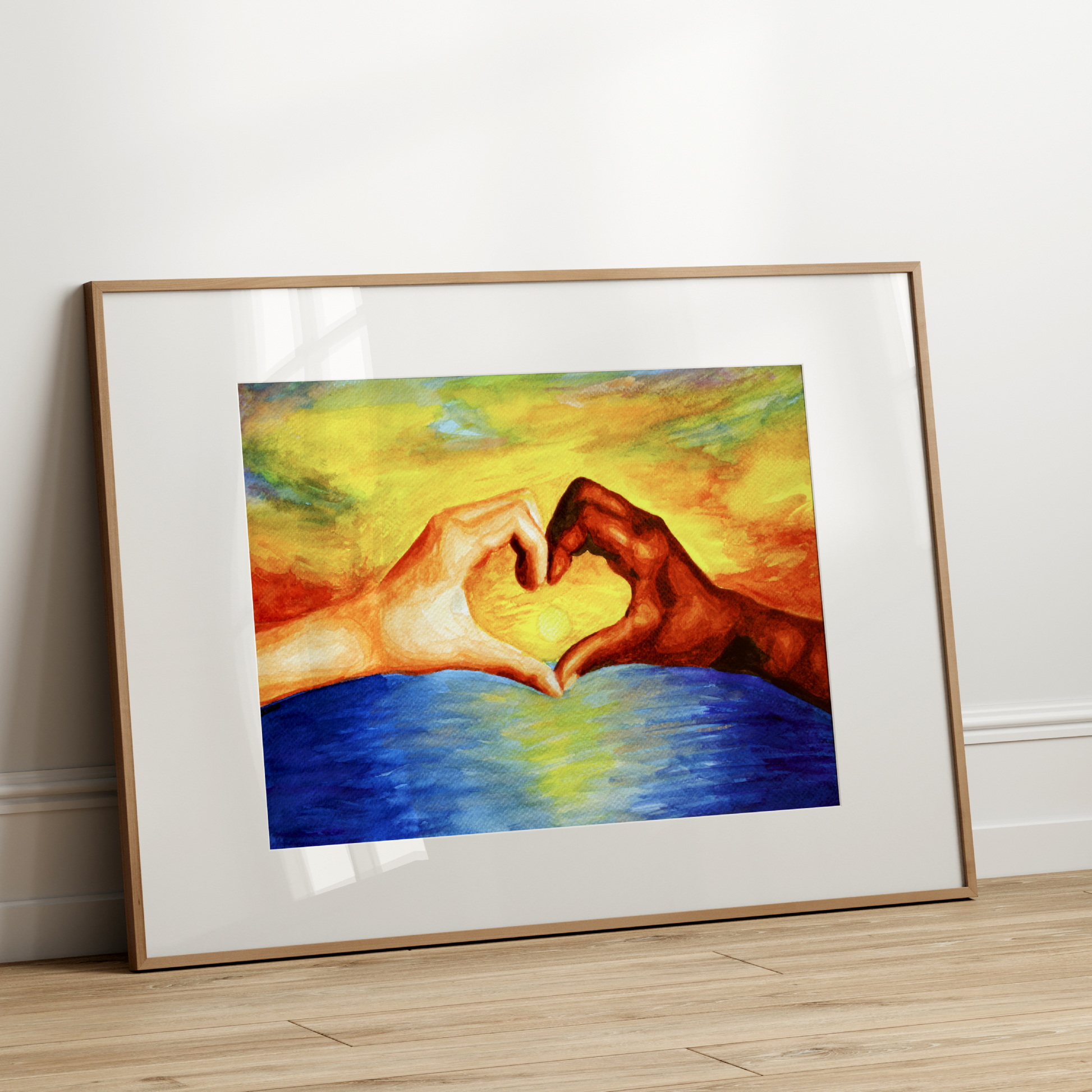 Framed artwork of two hands making a heart shape over water on a white wall.