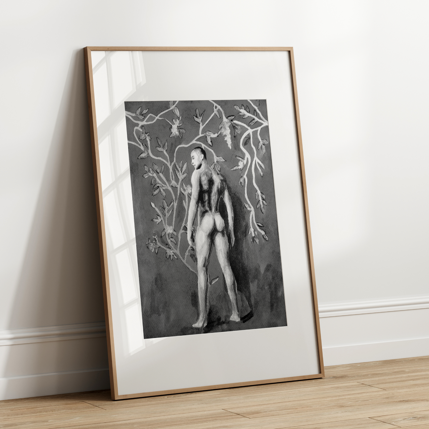 Framed black and white artwork of a nude figure with tree branches on a white wall.