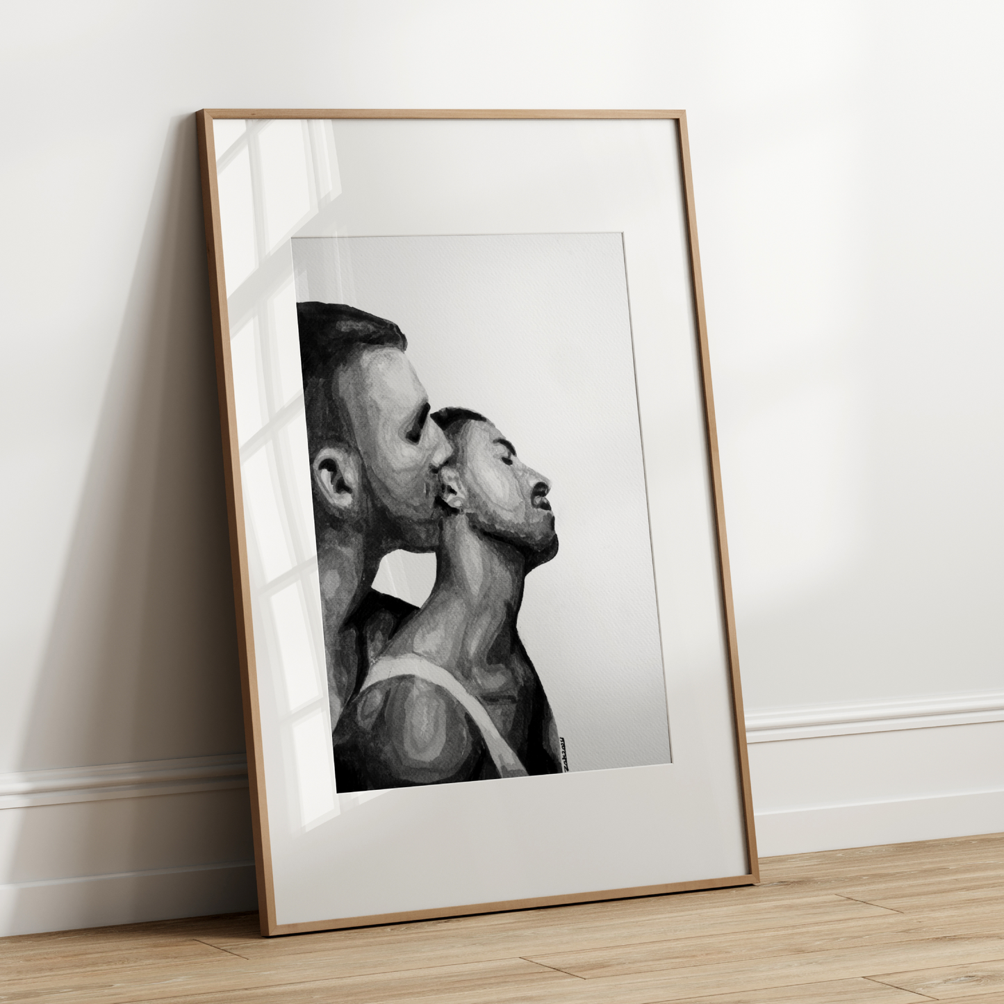 Framed black and white artwork of two men in a close embrace on a white wall.
