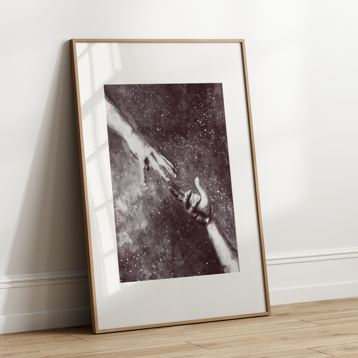 Framed artwork of two hands reaching towards each other on a white wall.
