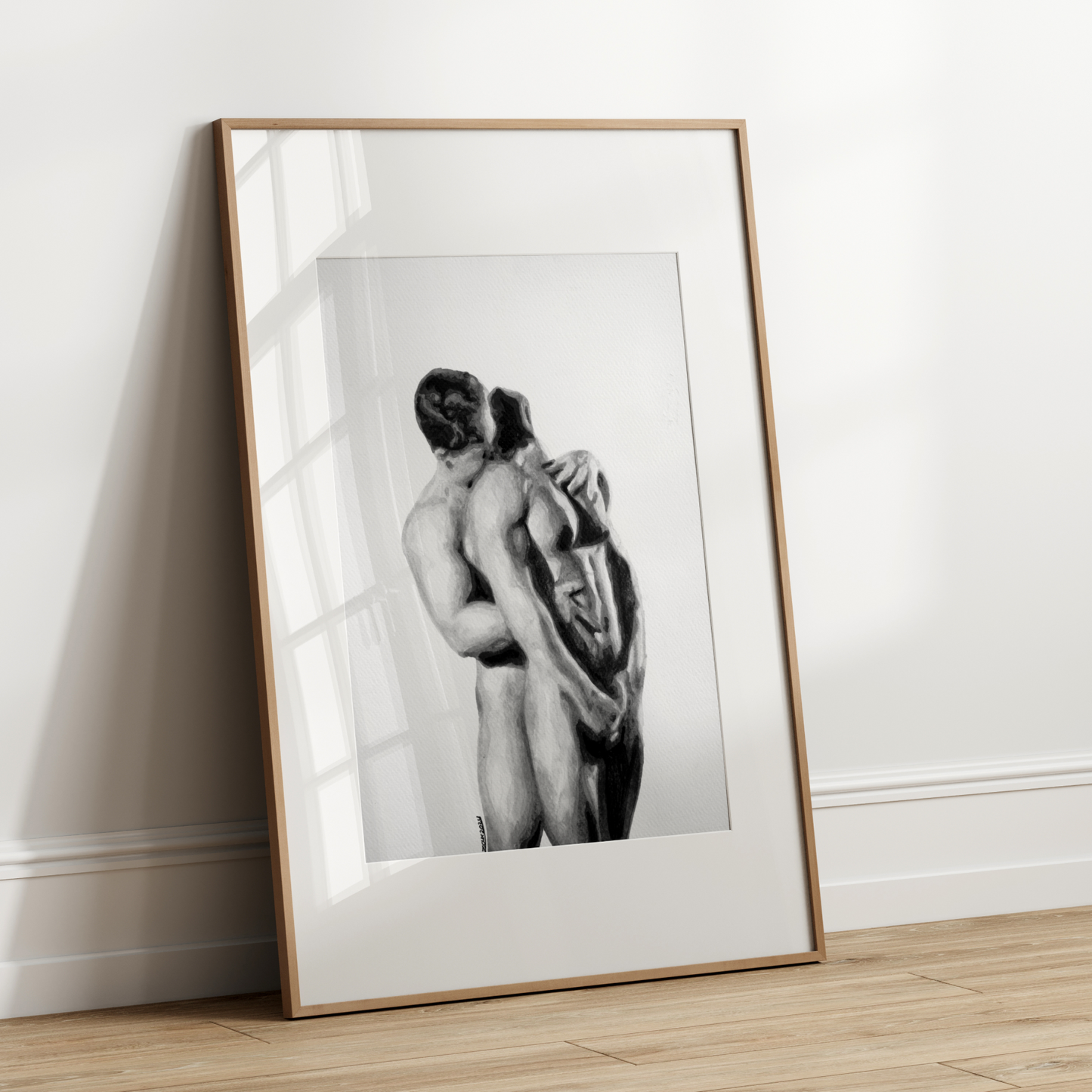Framed black and white artwork of two nude figures leaning against each other on a white wall.