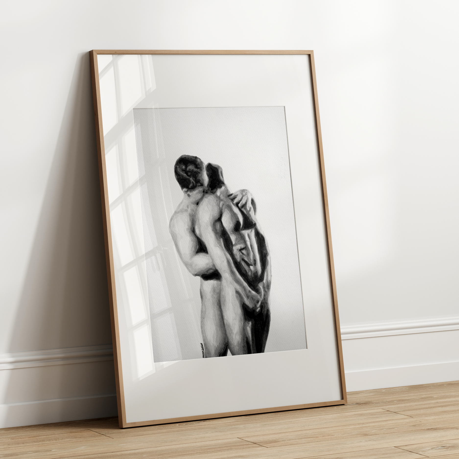 Framed black and white artwork of two nude figures leaning against each other on a white wall.