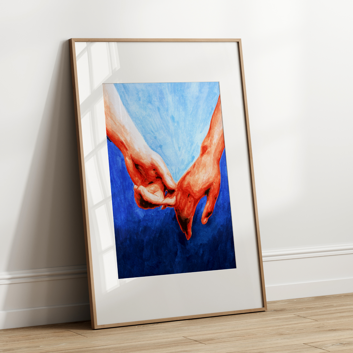 Framed artwork of two hands holding each other against a blue background on a white wall.