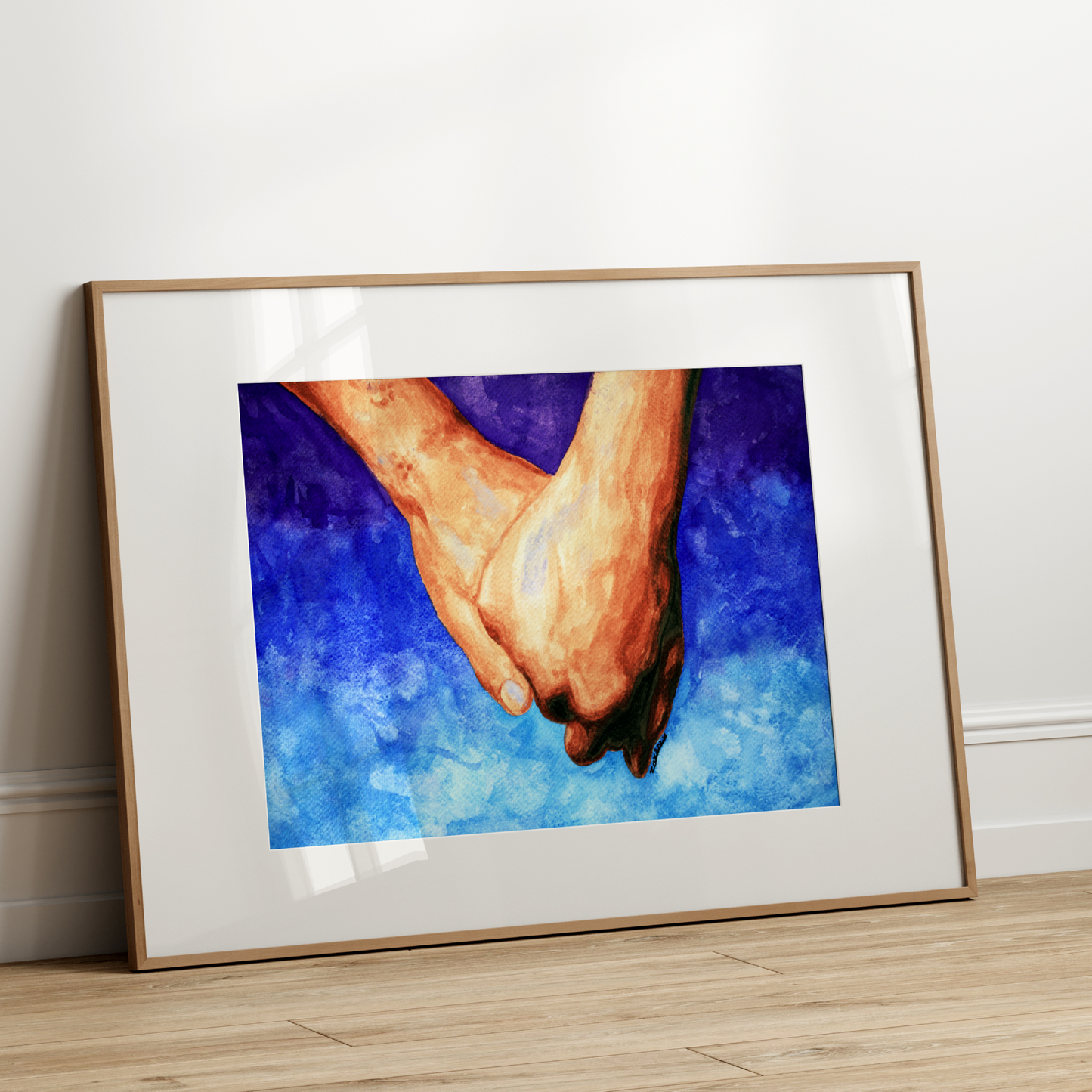Framed artwork of two hands holding a heart against a blue background on a white wall.