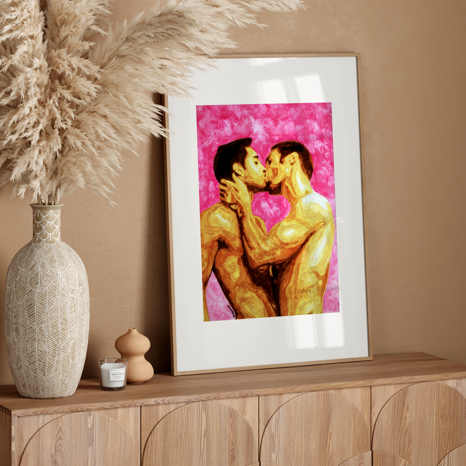 Framed artwork of two people kissing on a pink background, placed on a wooden surface with decorative items.