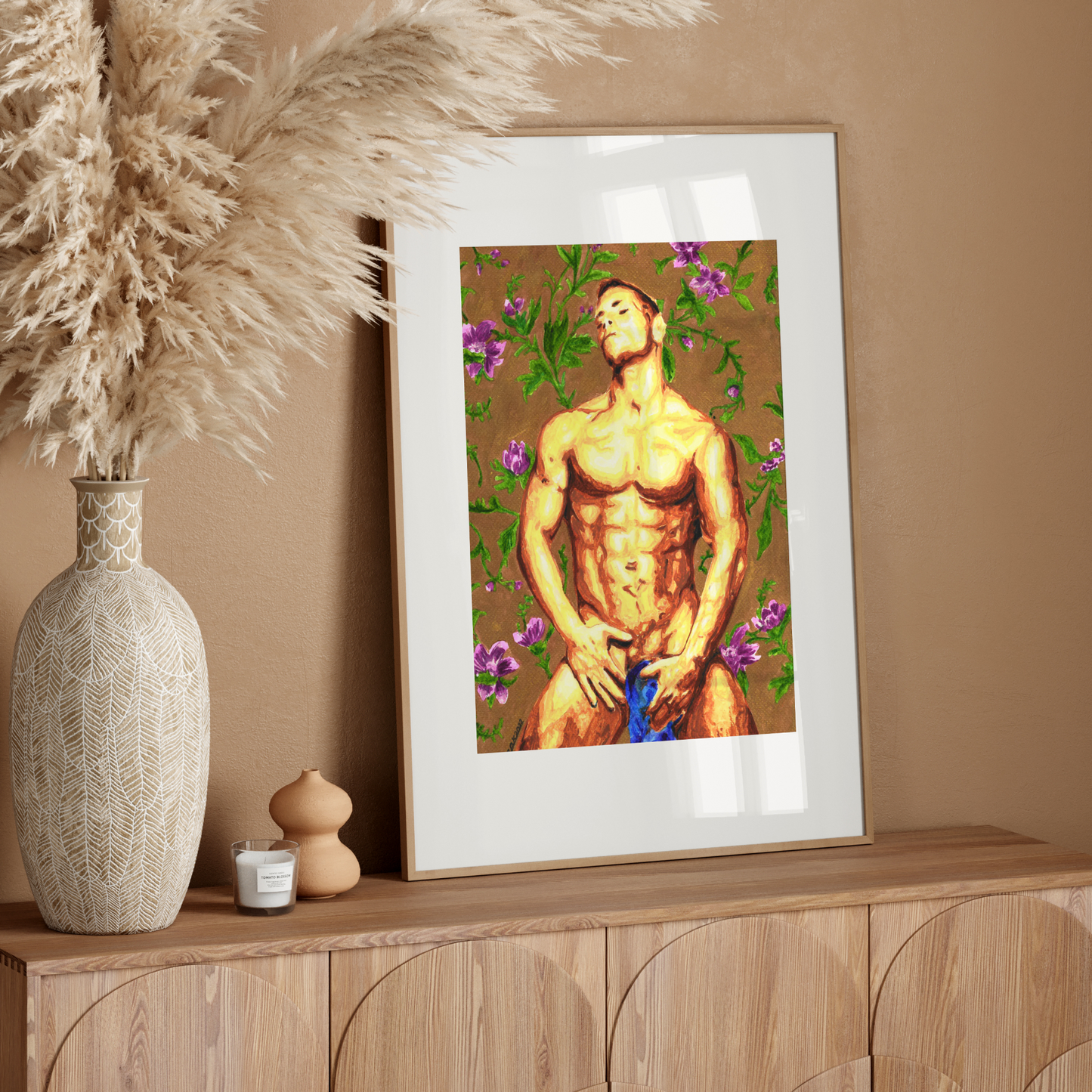 Framed artwork of a shirtless man with flowers on a wooden sideboard against a beige wall.